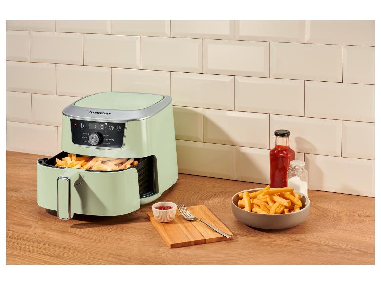 Lichtgroene airfryer met frietjes, ketchup en zout op een houten aanrecht.