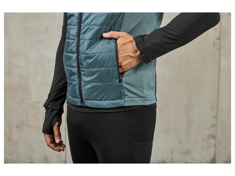 Een man draagt een blauwe gewatteerde vest en zwarte trainingsbroek.