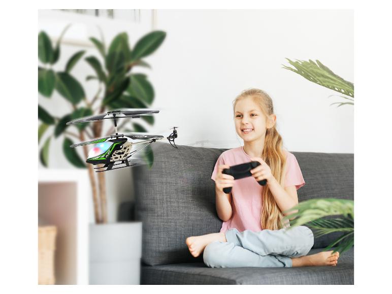 Lachend meisje op de bank bestuurt een op afstand bestuurbare speelgoedhelikopter.