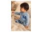 Baby in blauwe pyjama met Mickey Mouse-print, zittend op bed.