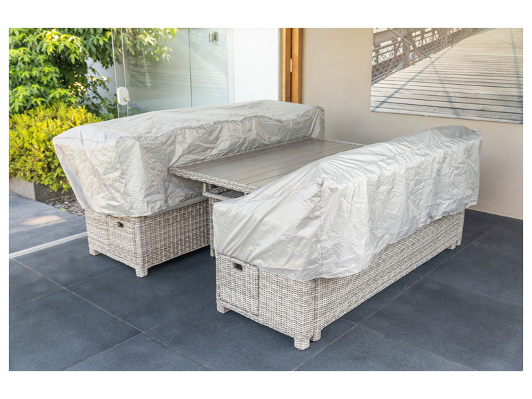 Een wicker loungeset met een tafel en twee stoelen, bedekt met een beschermhoes.