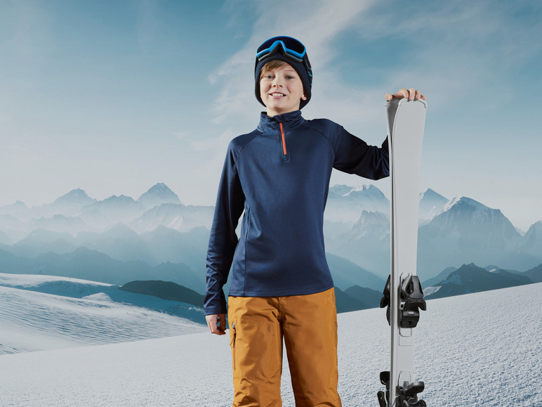 Een jongen met ski-uitrusting, inclusief ski's en een helm, voor een wintersportvakantie.