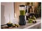 Zwarte blender met groene smoothie, fruit en kruiden in de keuken.