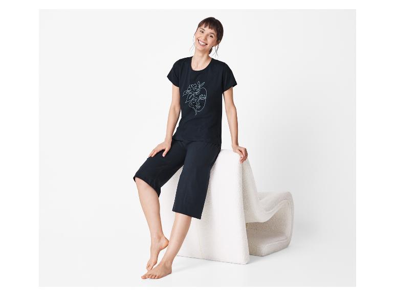 Vrouw in een zwarte pyjama met print zit op een witte poef.