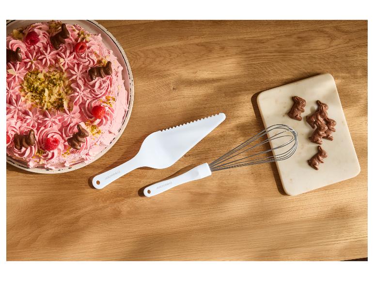 Roze taart met chocoladehaasjes, bessen en noten, witte taartschep en garde.