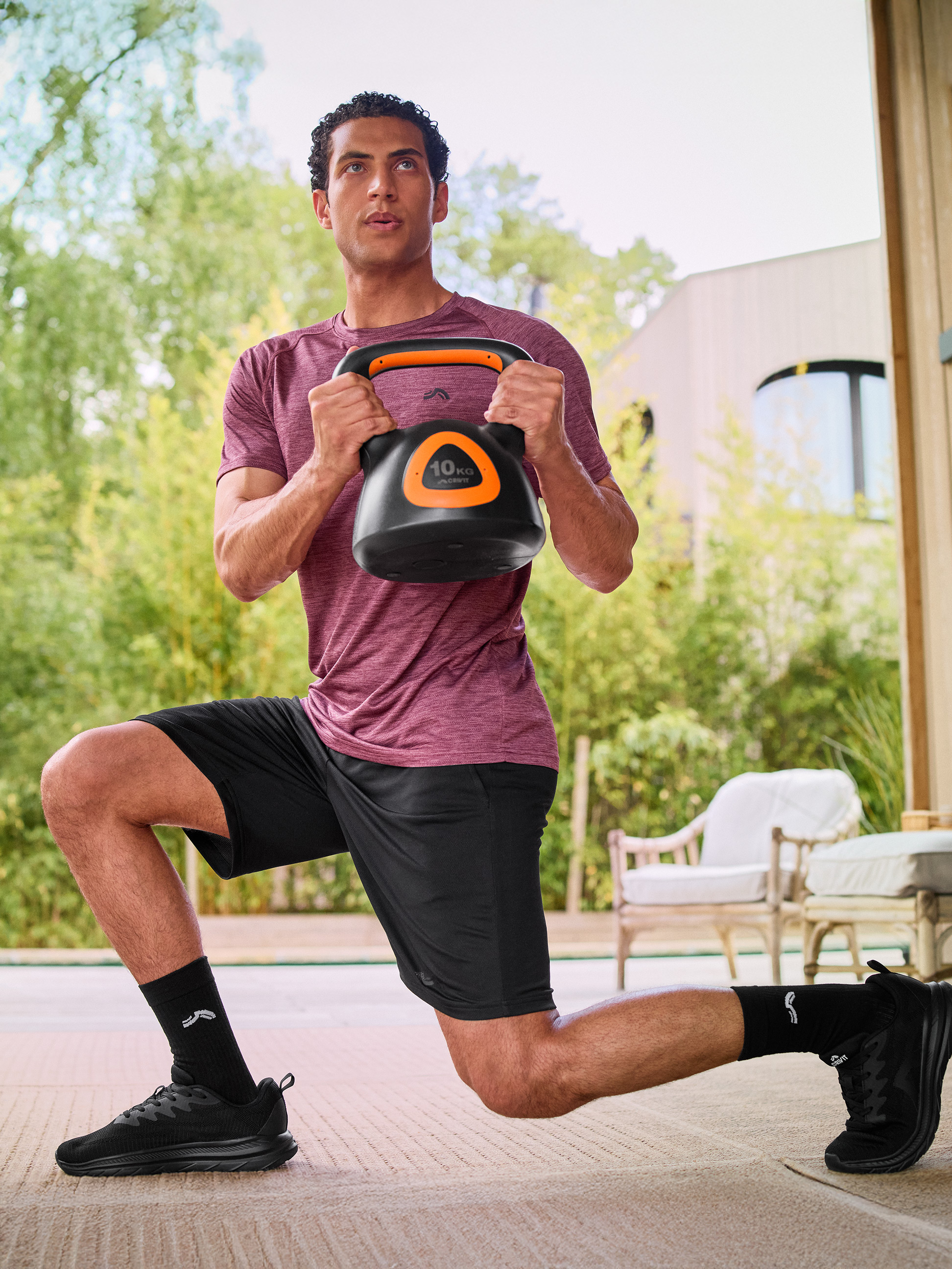 Man in sportkleding doet een lunge met een zwarte 10 kg kettlebell.