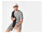 Man in gestreept T-shirt en korte broek, met witte pet en zwarte sweater over zijn schouder.