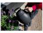 Persoon giet paarse bloemen water met een zwarte gieter.