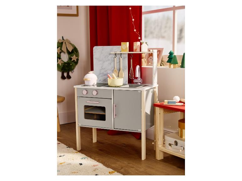 Grijze en witte houten speelkeuken met accessoires in een feestelijk versierde kamer.