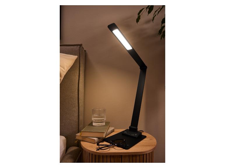 Zwarte tafellamp met verstelbare arm op een nachtkastje met boeken en een glas water.