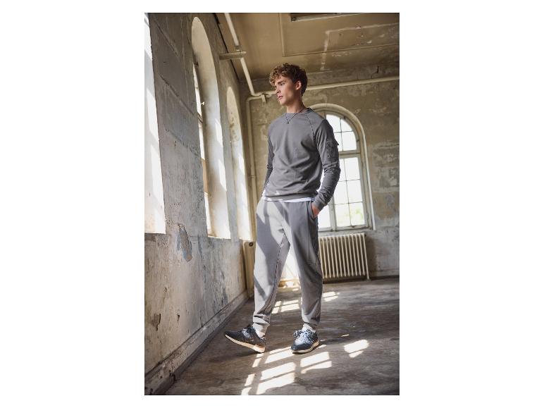 Man in grijze sweater en New Balance joggingbroek staat in een verlaten gebouw.