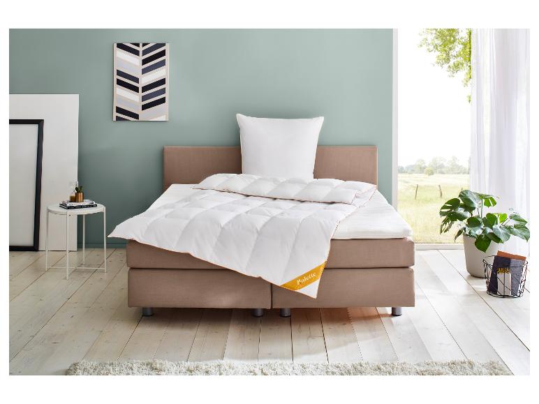 Bed met wit dekbed en kussen, nachtkastje en plant in een lichte slaapkamer.