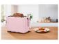 Roze broodrooster met twee sneetjes geroosterd brood en een bord met tomaat-basilicumtoast.