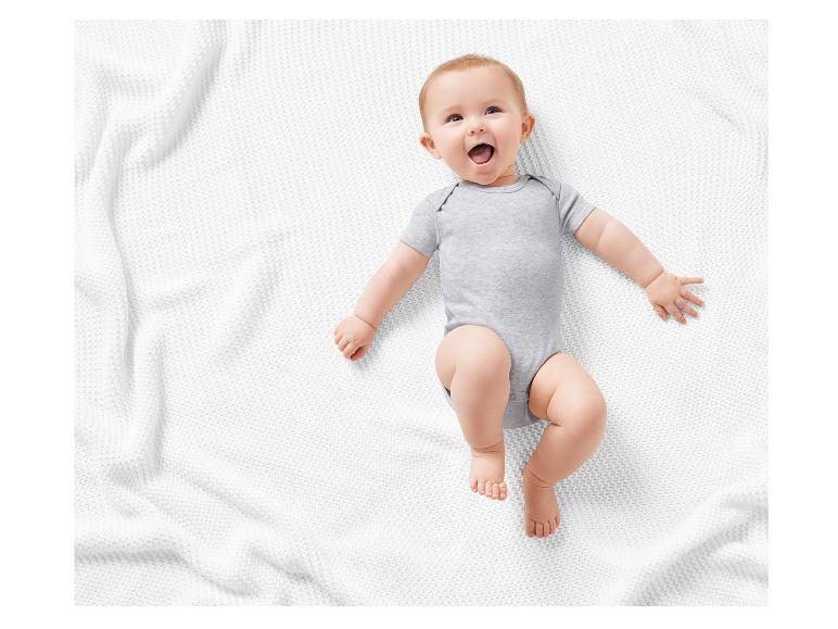 Lachende baby op een wit kleedje, in een grijze romper.