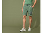 Man draagt groene shorts met 'United Club' print en witte sneakers.