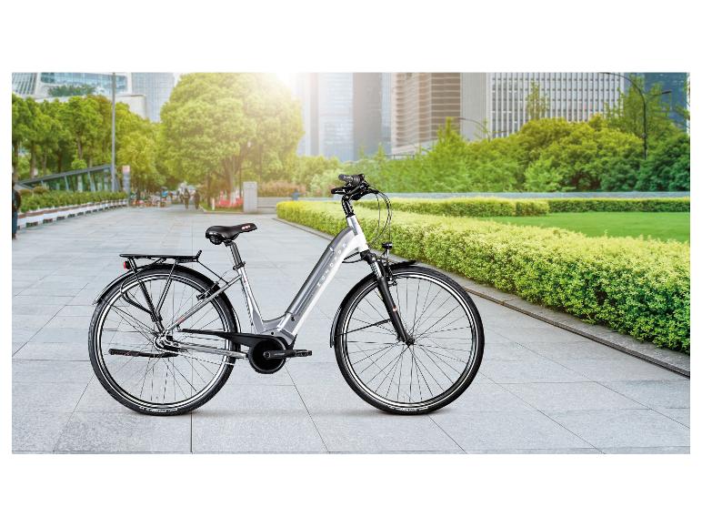 Zilveren Zündapp e-bike op een betegeld pad met een stadspark op de achtergrond.