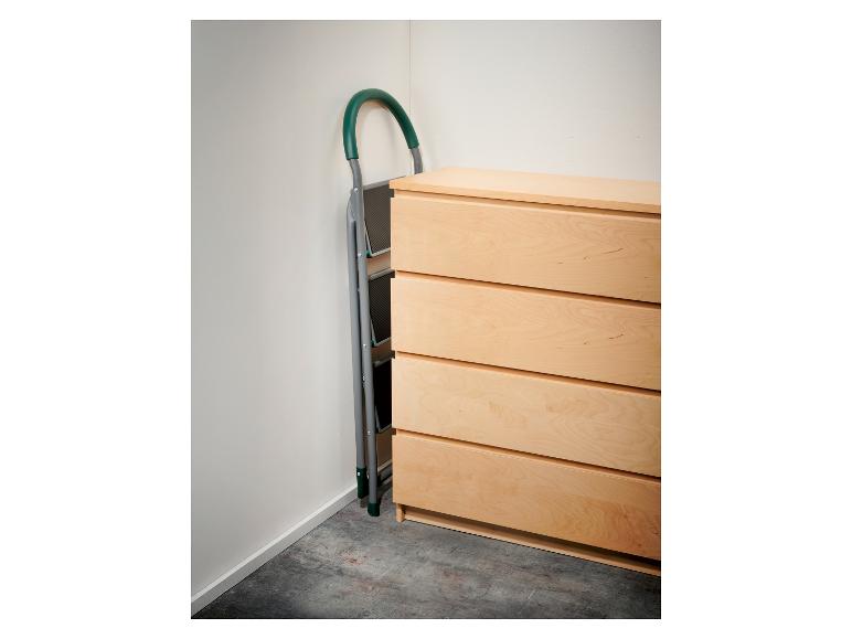 Een opvouwbare trapladder met groen handvat staat naast een lichte houten ladekast.