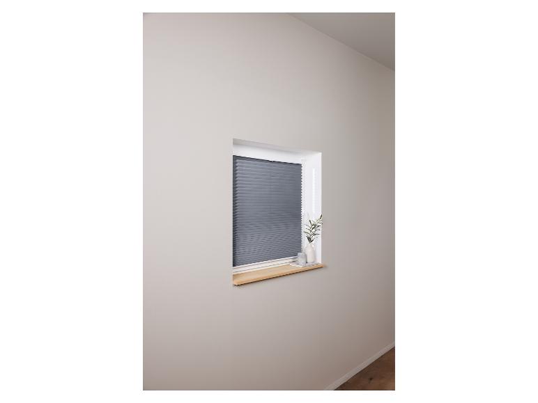 Grijze plisségordijnen in een lichte kamer.