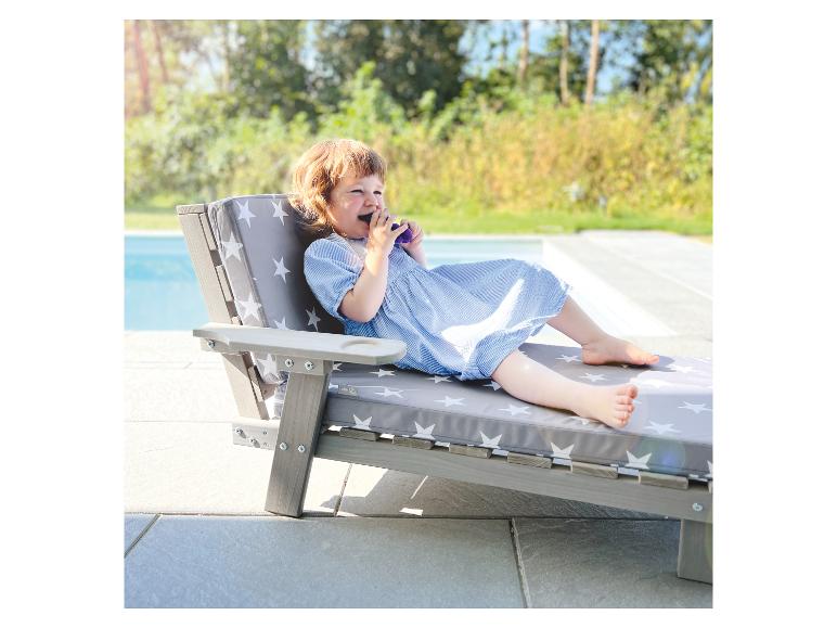 Klein kind in blauwe jurk ontspant op een ligstoel met sterrenpatroon bij het zwembad.