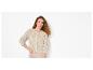 Vrouw met krullend haar draagt een beige opengewerkt gebreid vest en een beige broek.