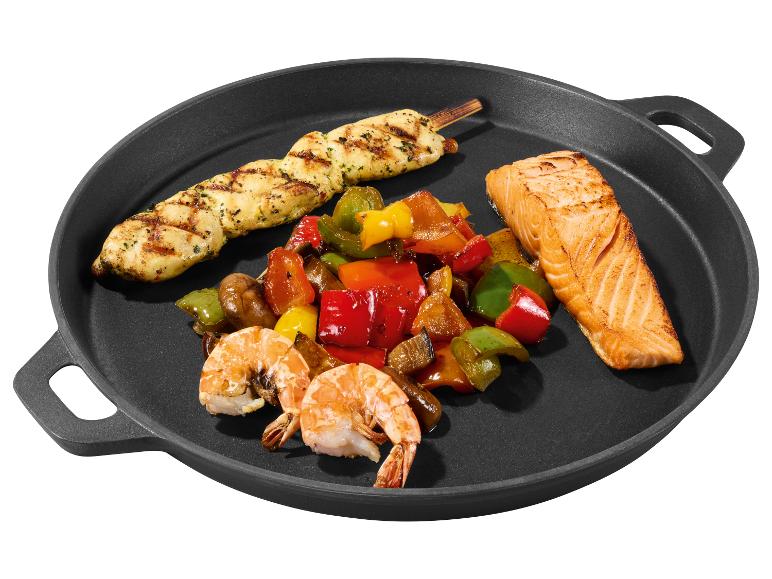 Gegrilde kipsaté, zalmfilet, garnalen en kleurrijke paprika's in een zwarte pan.