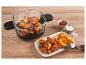 Glazen airfryer met kipvleugels en aardappelpartjes, ketchup en zout op een houten tafel.