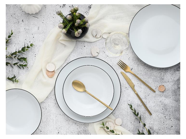 Tafeldekking met witte borden, goudkleurig bestek, glas en groene takken op grijze achtergrond.