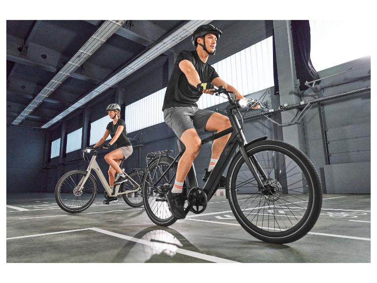 Twee fietsers op elektrische fietsen, met helmen en sportkleding in een parkeergarage.