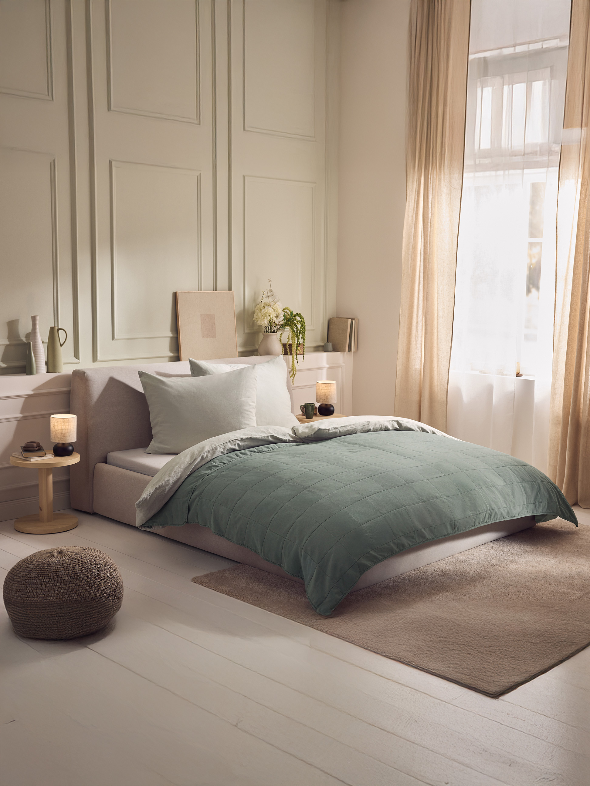 Slaapkamer met tweepersoonsbed, groen dekbed, witte kussens en houten nachtkastje.