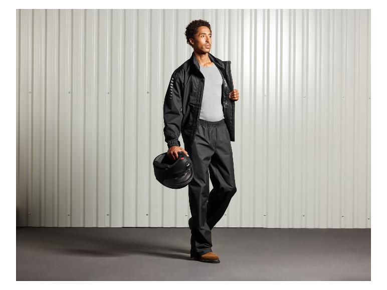 Man in zwarte regenjas en broek met een helm in zijn hand.