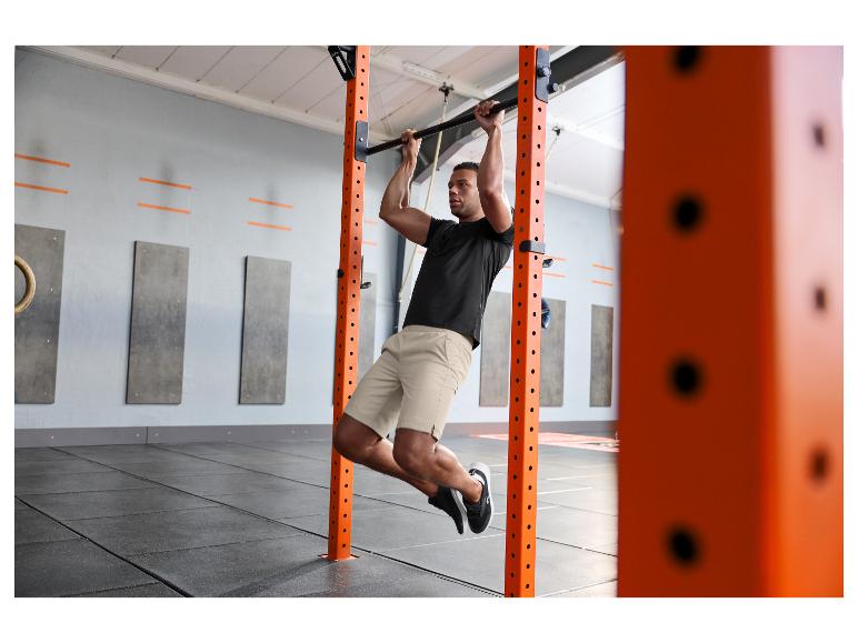 Man in zwart t-shirt en beige korte broek doet pull-ups in een sportschool.