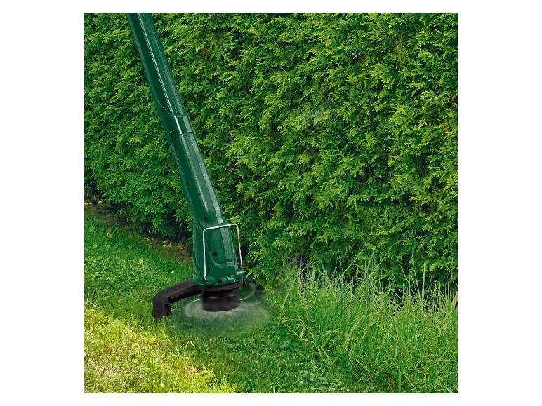 Grastrimmer in actie, snijdt hoog gras naast een heg.