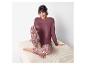 Vrouw in bordeauxrode pyjama en een patroonbroek zit op een lichte ottomane.