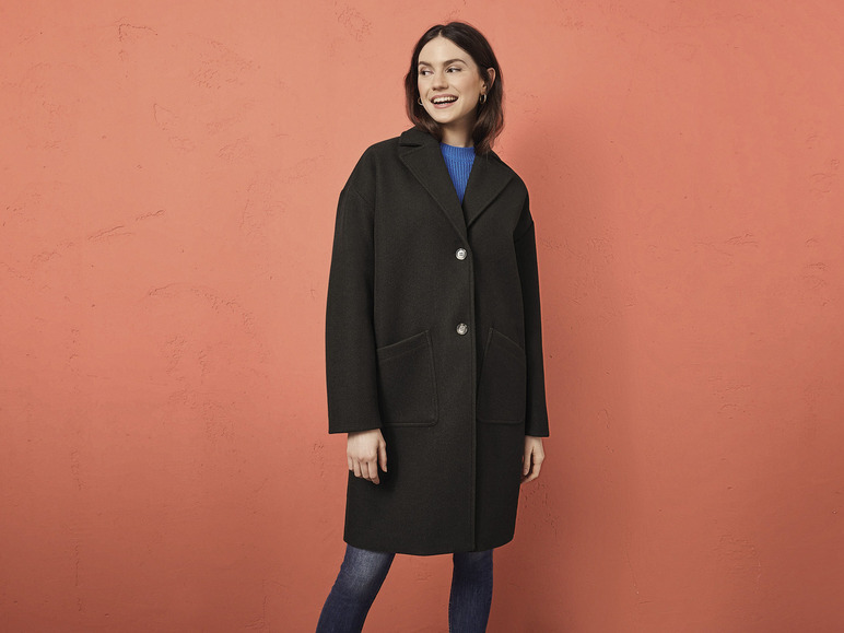Een vrouw draagt een zwarte jas en blauwe jeans.