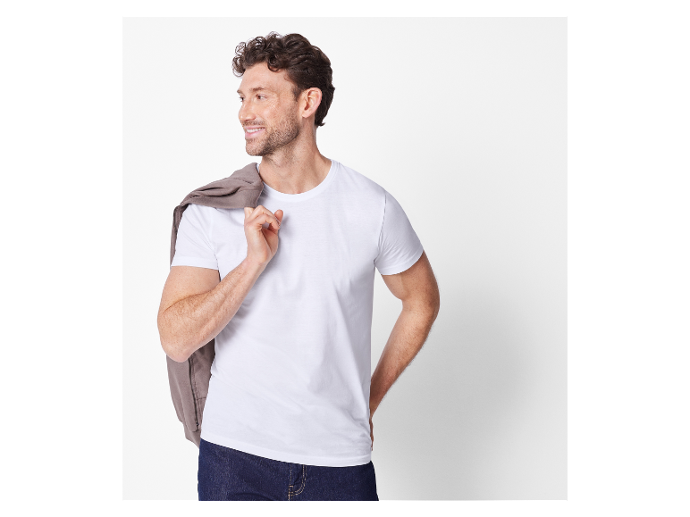 Lachende man in wit t-shirt en bruine jas over zijn schouder.