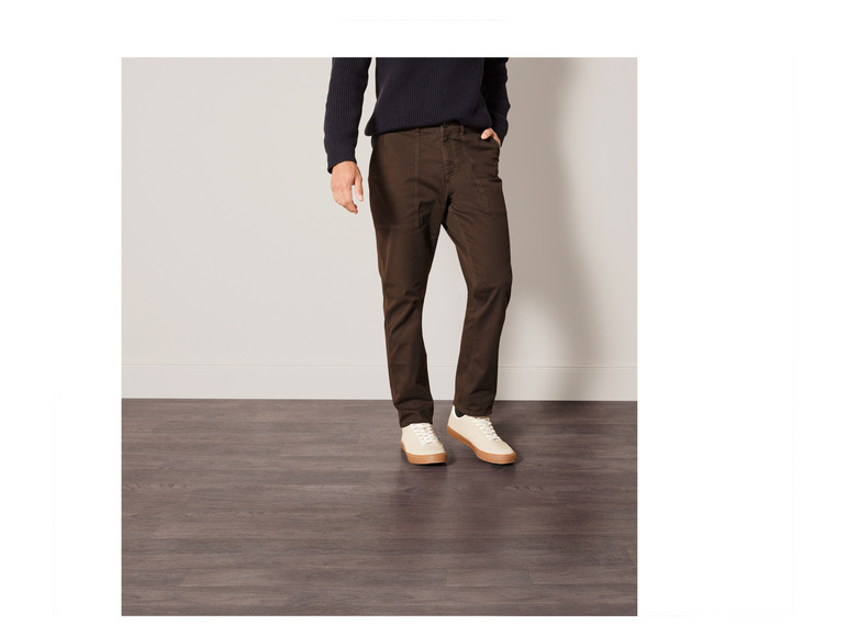 Man draagt donkerbruine chino's met witte sneakers.