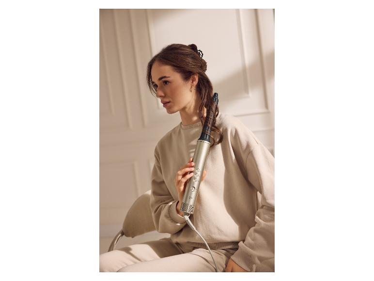 Vrouw houdt een Cien föhnborstel in haar haar, gekleed in een beige trainingspak.