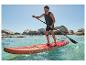 Man op rood SUP-board peddelend in zee, met rotsen op de achtergrond.