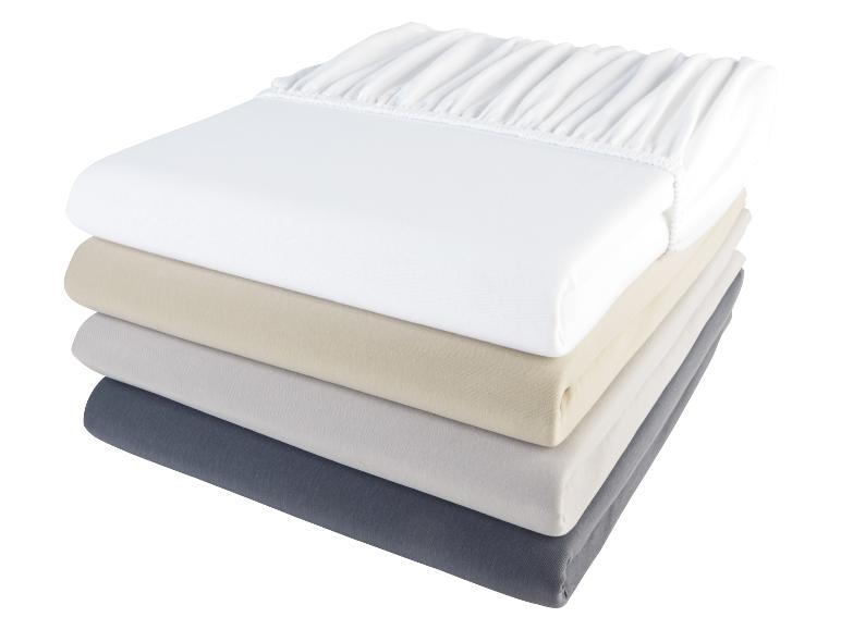 Een stapel witte, beige, grijze en donkergrijze hoeslakens.