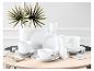 Wit servies met borden, kommen en mokken op een lichte houten tafel.