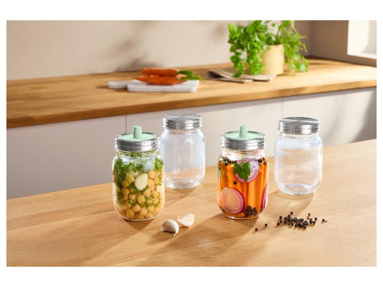Glazen potten met metalen deksels en fermentatieventielen, met kikkererwten en ingelegde wortels.