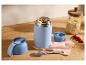 Blauwe voedselthermos met granola, lepel en haver op een houten ondergrond.