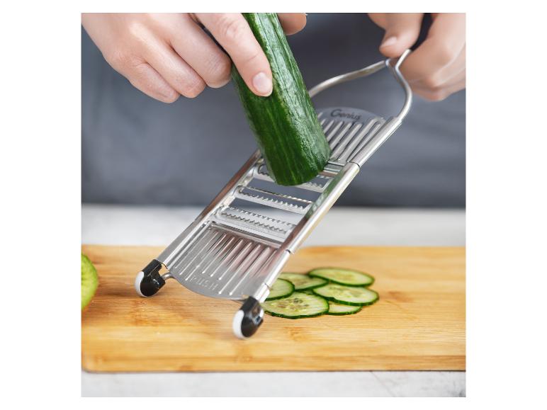 Handen snijden komkommer met een Genius mandoline op een houten snijplank