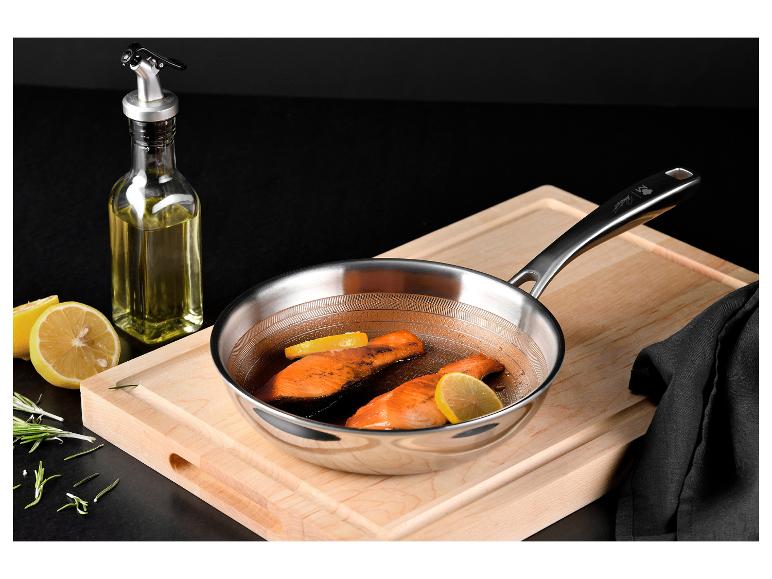 Roestvrijstalen pan met zalm en citroen op een houten snijplank.