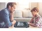 Een vader en zoon spelen op een elektronisch schaakbord aan een houten tafel.