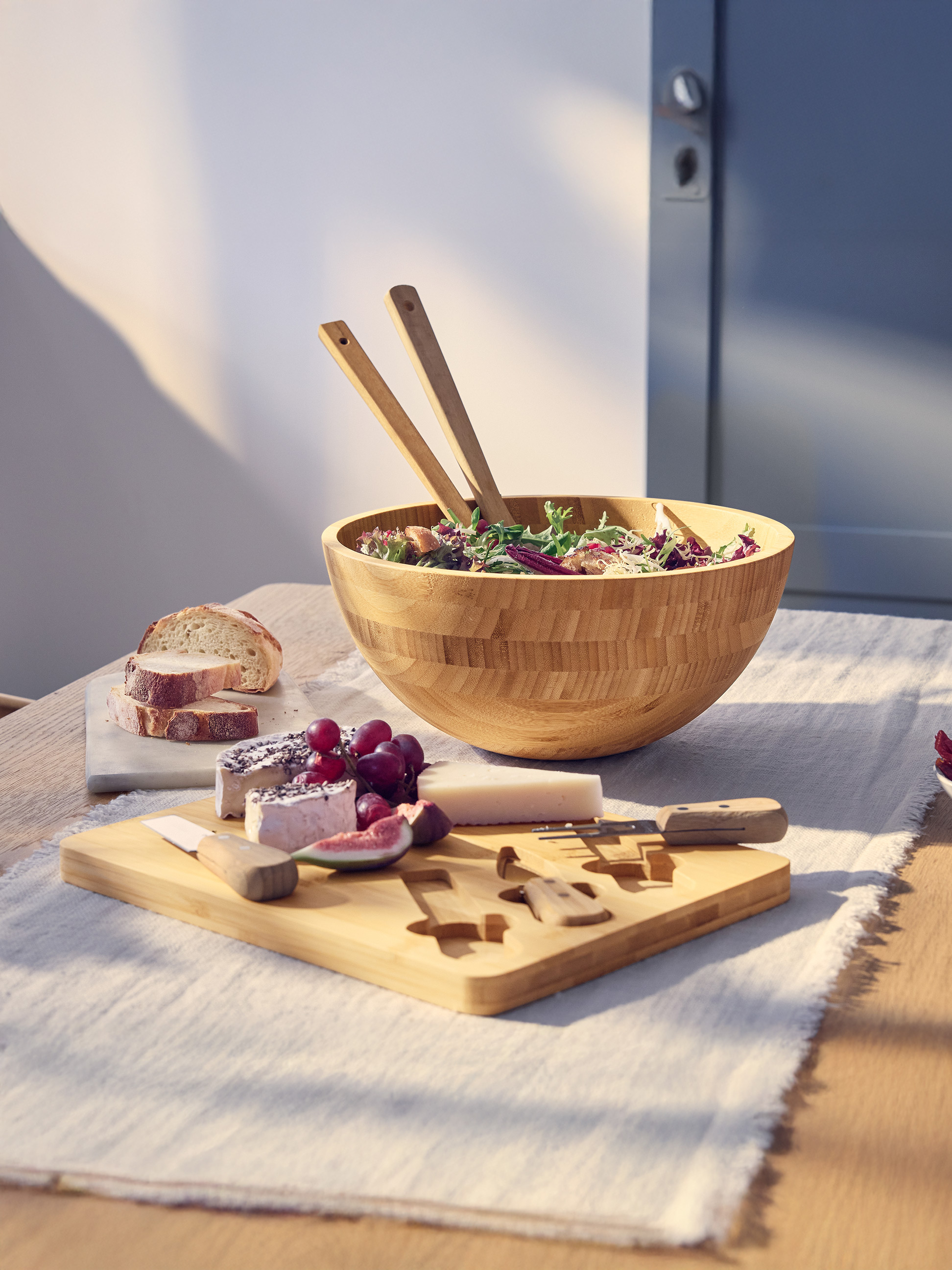 Salade in houten kom met bestek, kaasplank met brood en fruit.