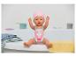 Babypop in roze zwempak en muts, zittend op de rand van een bad met handdoeken.