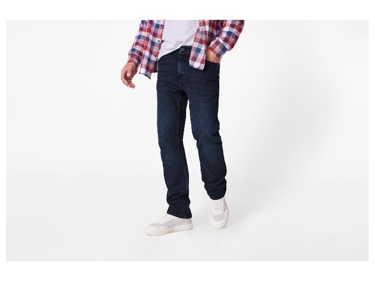 Man draagt donkerblauwe jeans, een wit T-shirt en een geruit overhemd.