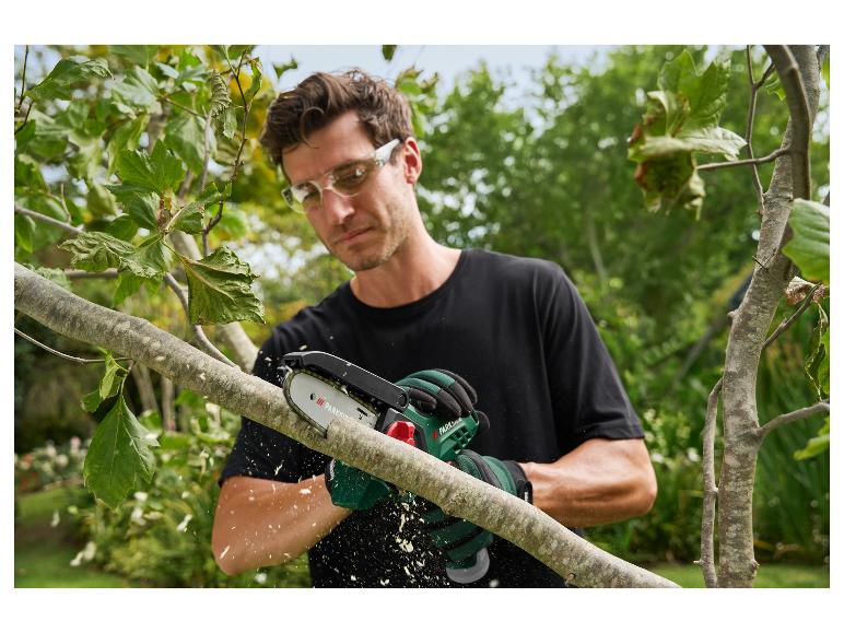 Man snoeit een boomtak met een kettingzaag, met veiligheidsbril en handschoenen.