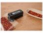 Zwarte zakken sealer met gemalen chili in een zak en een kom op een houten tafel.